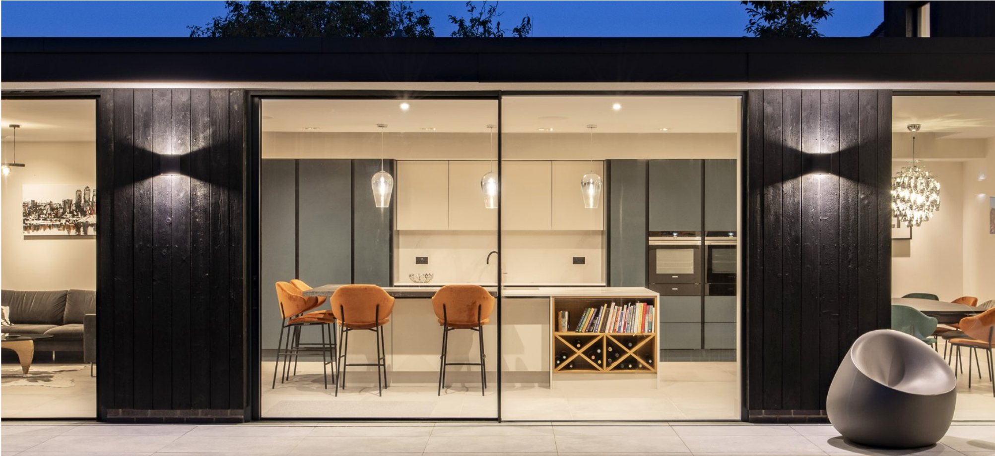Three-panel Cortizo COR Vision sliding door opening a kitchen to the garden at dusk